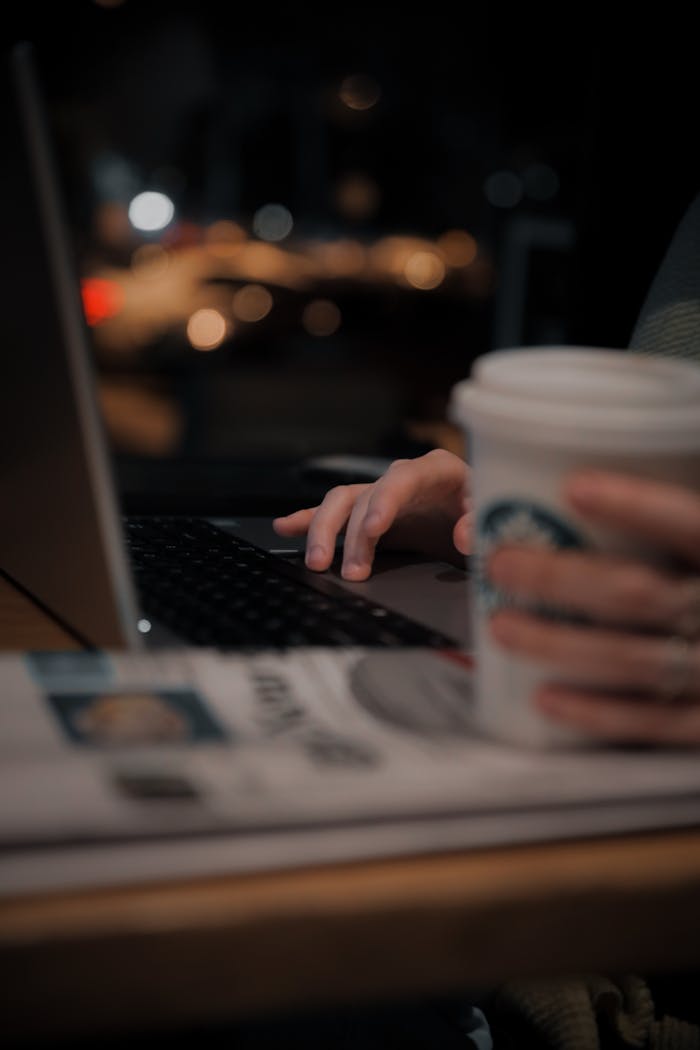 A person using a laptop in a dimly lit coffee shop, enjoying a warm drink.