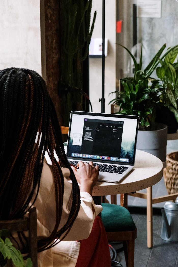 A businesswoman using a laptop at a café, surrounded by plants and modern decor.